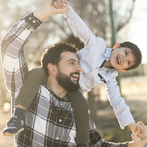 Adult man smiling with his son on his shoulders.